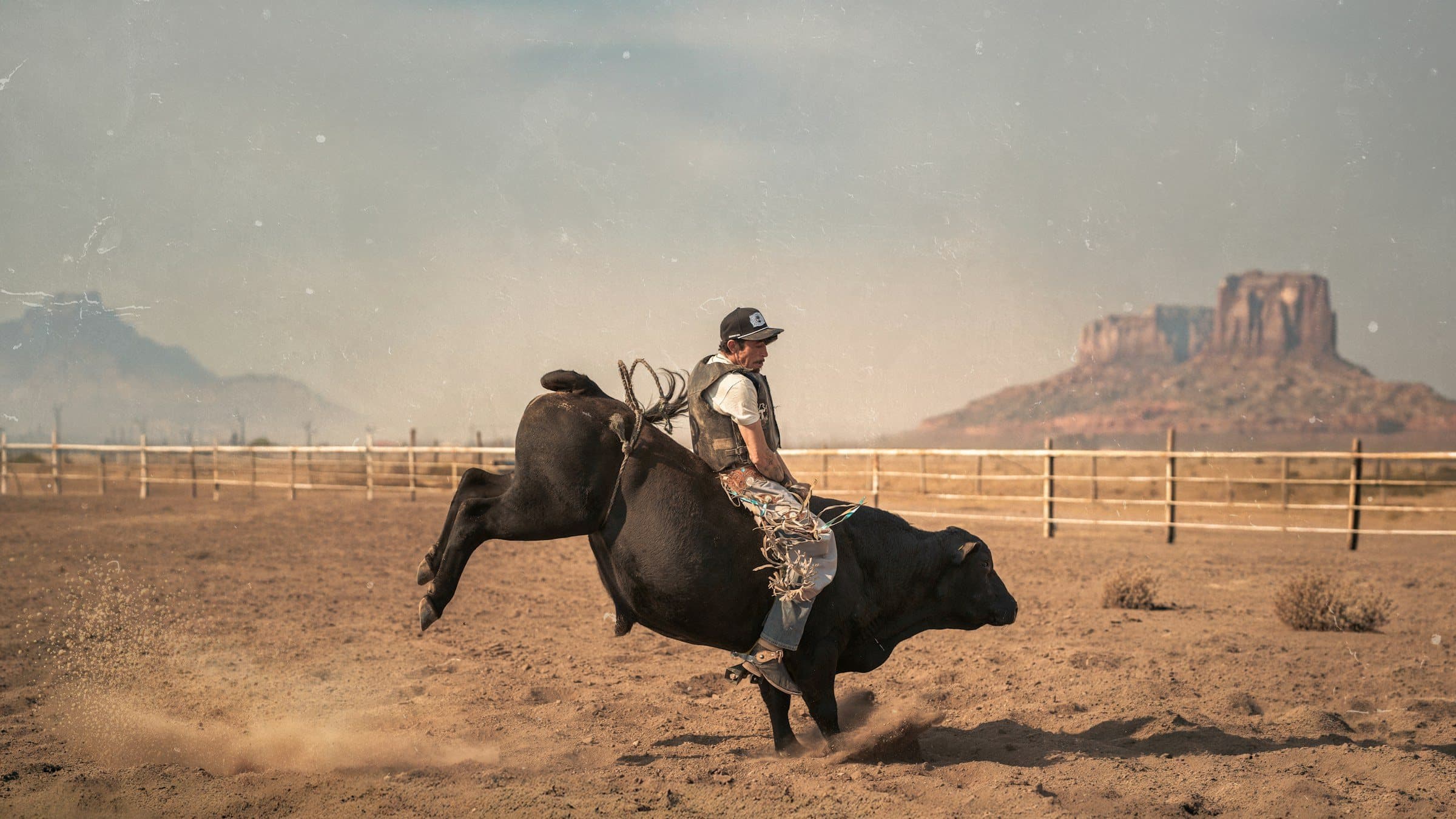 A bull rider in a desert arena, mesas behind.
